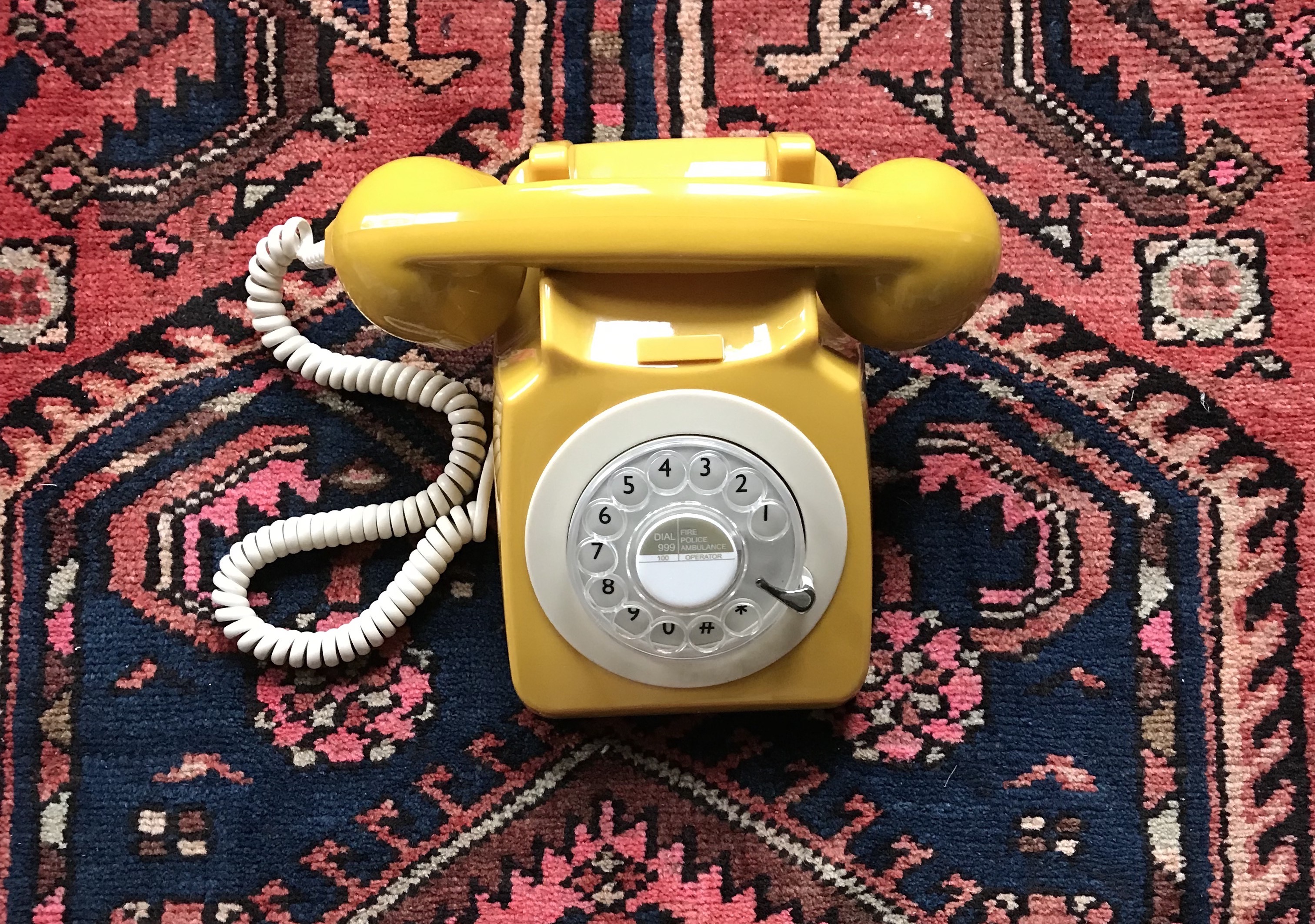 Old-school yellow rotary phone on carpet.
