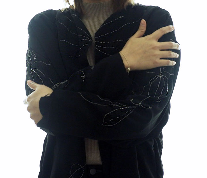 Person wearing embroidered jacket, hugging themselves.