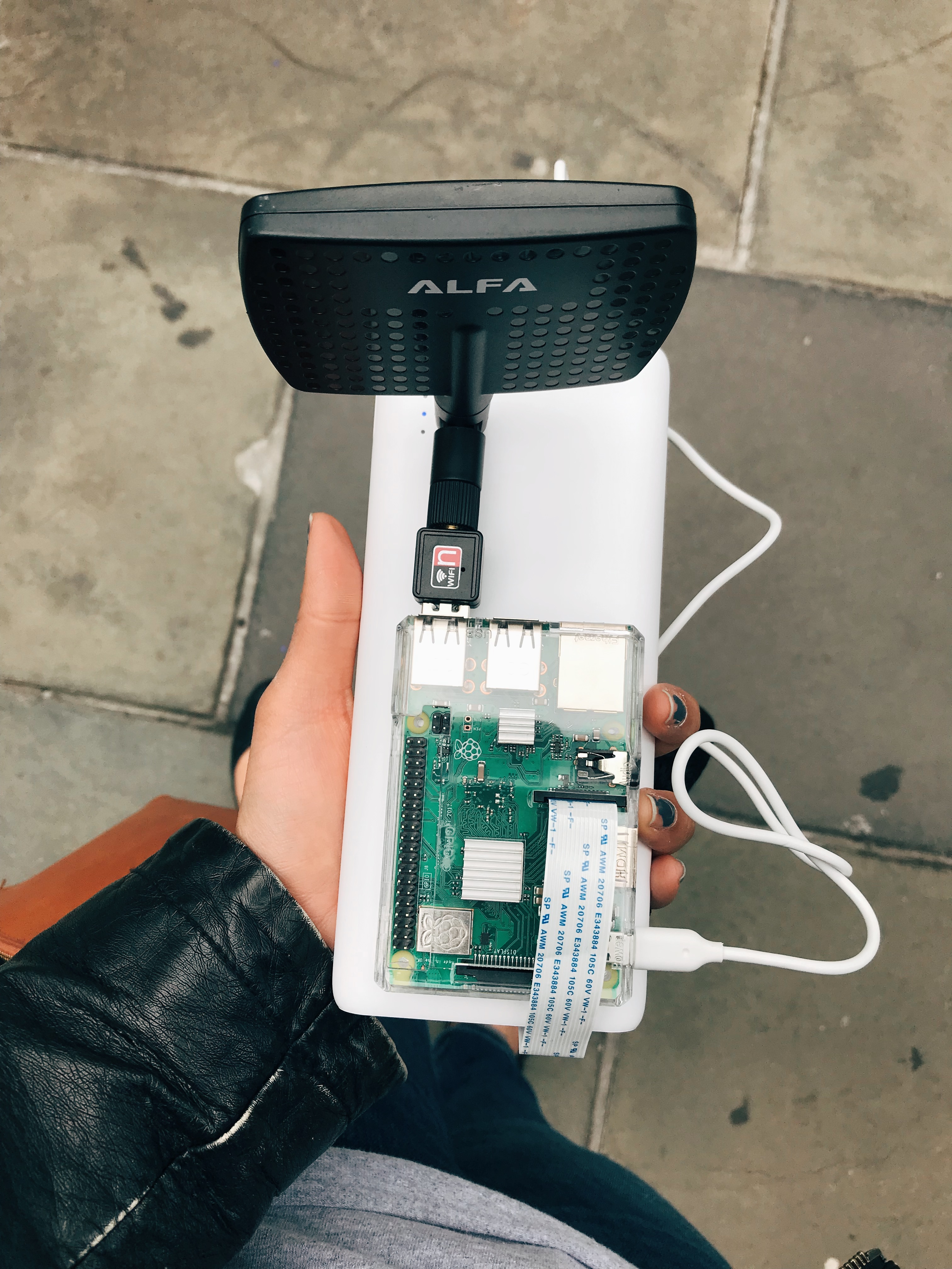 A hand holding a portable battery device and a raspberry pi with WiFi antenna attached.